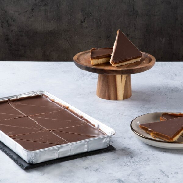 Chocolate caramel shortbread slices with a chocolate topping on a cake stand and plate.