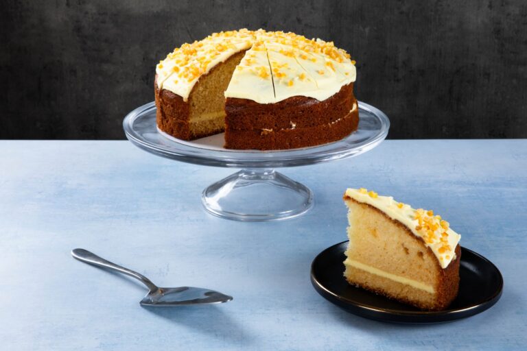 Orange drizzle cake with creamy frosting and orange zest on a glass cake stand.